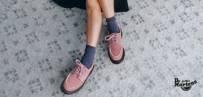 Person sitzt im Schneidersitz auf dem Teppich, hält einen Blumenstrauß, trägt pinke Dr. Martens Schuhe und graue Socken.