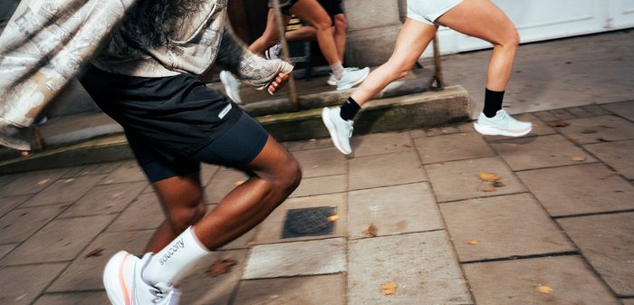 Two people running energetically on a city sidewalk wearing athletic shoes and casual sportswear.