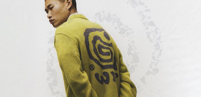 Suéter de punto en verde olivo con un gran diseño de espiral negra en la parte posterior. Cuenta con un cuello tipo chal y puños acanalados. Tela texturizada.