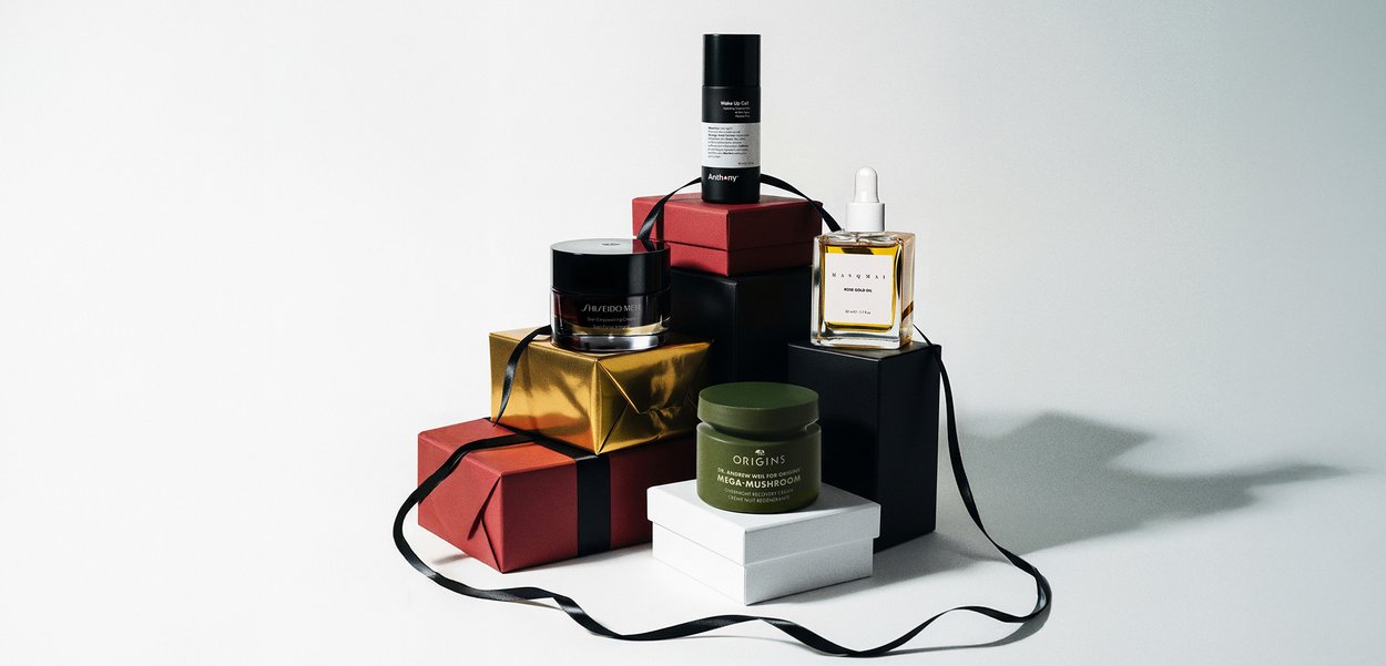 Hudpleiebeholdere på stablede røde, gull-, svarte og hvite gaveesker med svarte bånd på en lys bakgrunn.