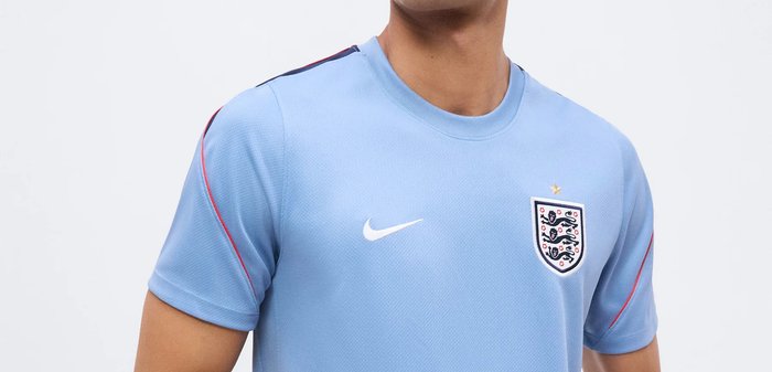 Homme portant un maillot de football d'Angleterre bleu clair avec le logo Nike et le blason de l'Angleterre, montrant le haut du torse et le cou.