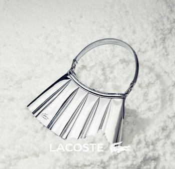 Silver pleated handbag with a smooth texture and a short handle. Features a Lacoste logo and distinct folding design.