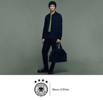 Jonge man in een donkere jas en broek die een grote zwarte sporttas vasthoudt, staande voor een grijze achtergrond met de logo's van de Deutscher Fußball-Bund en Marc O’Polo.