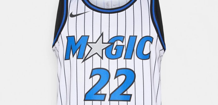 Μπασκετική φανέλα σε λευκό με μαύρες και μπλε λεπτομέρειες. Διαθέτει κάθετες ρίγες, το όνομα "MAGIC" σε μπλε και τον αριθμό "22" στο μπροστινό μέρος. Παρουσιάζεται το λογότυπο της Nike.