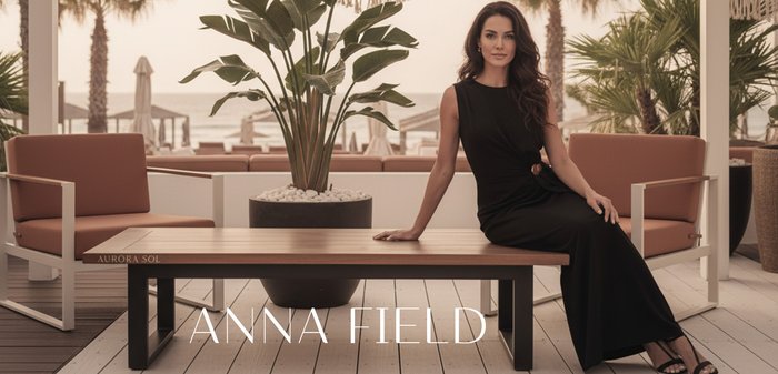 Mujer con un vestido negro sentada en un banco de madera en un patio con plantas y palmeras de fondo.