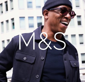 Ciemnogranatowa kurtka z dwoma przednimi kieszeniami i zapięciem na guziki, noszona na czarnej koszuli. Okrągłe okulary przeciwsłoneczne, materiał o strukturze, tło miejskie.