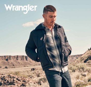 Svart isolert jakke med hette, glidelås foran og sidelommer over en rutete skjorte, kombinert med mørke jeans mot et steinete landskap.