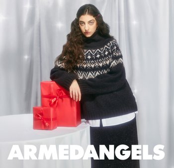 Chunky knitted sweater in dark navy with white geometric patterns, paired with a long black glittery skirt; two red gift boxes beside a table.