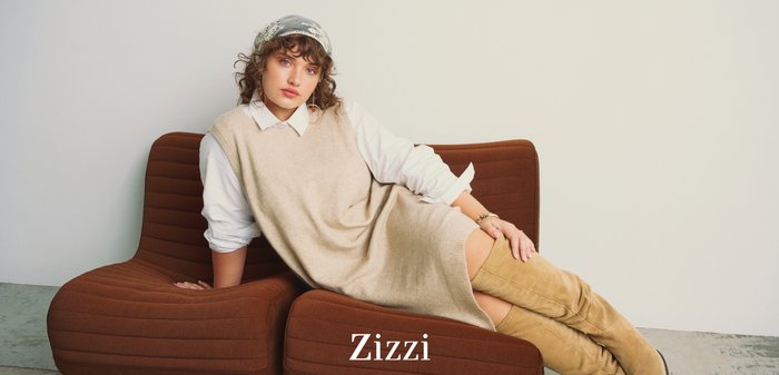 Pull sans manches beige porté sur une chemise blanche, assorti à des bottes hauteur cuisse couleur fauve, assis sur une chaise marron texturée aux formes courbes.