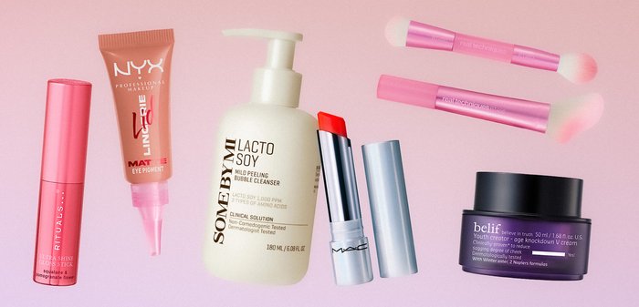 Divers produits de beauté sur un fond rose comprenant du gloss à lèvres, du pigment pour les yeux, un nettoyant, un rouge à lèvres rouge, des pinceaux pour les yeux et une crème pour le visage.