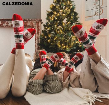 Des chaussettes rouges et blanches arborant un motif de pain d'épice avec des accents verts. Portées par plusieurs personnes, elles sont présentées devant un sapin de Noël.