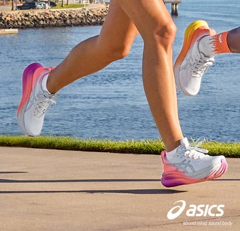 Twee mensen rennen langs het water, met witte Asics-sneakers met kleurrijke zolen, op een geplaveid pad vlak bij het gras.