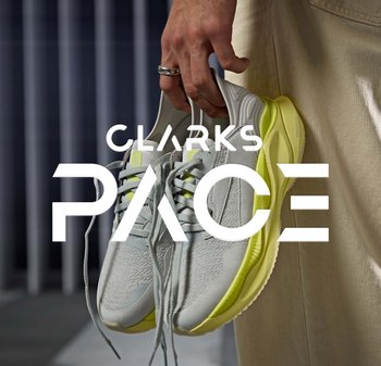 Baskets de sport gris clair avec une tige texturée, des accents jaunes et une semelle flexible, tenues par une main. Marque : Clarks Pace.