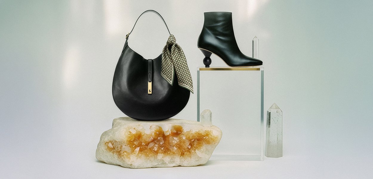 Črna usnjena ročna torbica z vzorčasto rutko, kombinirana s črnim gležnjarjem z edinstvenim ukrivljenim peto. Izpostavljeno na mineralni podlagi.