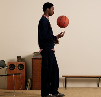 Casualny strój z granatowym swetrem, kołnierzykiem w czerwone paski i ciemnymi dżinsami. Równoważenie pomarańczowej piłki koszykowej podczas stania obok krzesła i stosu płyt.
