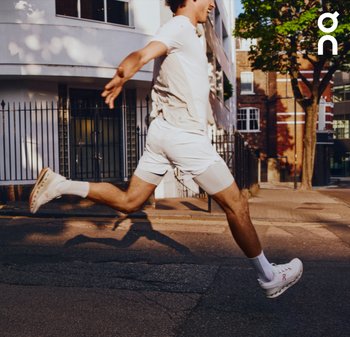 Baskets de sport blanches avec une semelle rembourrée, affichant un design épuré et un branding discret, associées à un short et un haut assortis clairs.