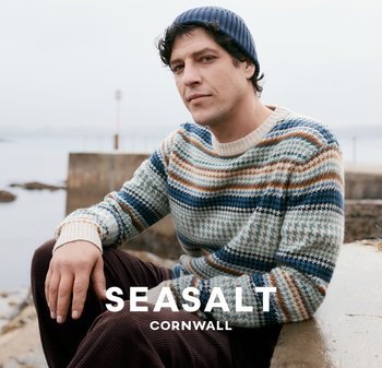 Pletený svetr s vícebarevnými horizontálními pruhy v modré, béžové a hnědé barvě, s žebrovaným kulatým výstřihem. Nosený s tmavou čepicí.