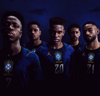 Cinque calciatori maschi indossano maglie della nazionale brasiliana di colore blu scuro e stanno in fila contro uno sfondo scuro, con espressioni serie rivolte in avanti.