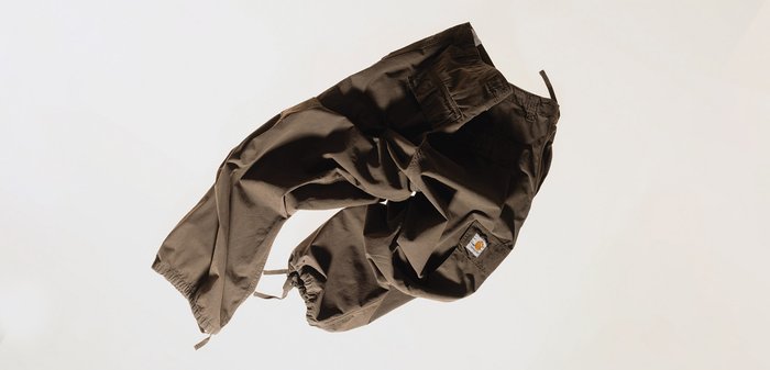 Pantalones marrones elásticos con puños y cintura elásticos, con bolsillos y una etiqueta con el logo. La tela parece ligera y con textura.