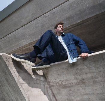 Sneaker neri e bianchi con suole testurizzate, giacca di jeans blu e pantaloni di jeans scuri contro uno sfondo di cemento.