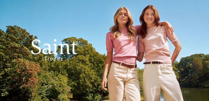 T-shirt bleu clair posé sur une rambarde de pont en métal rouillé donnant sur une rivière calme avec des arbres aux couleurs d'automne. Le texte dit "Saint Tropez."