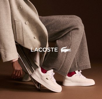 Zapatillas de cuero blancas con acentos en rosa, que presentan perforaciones y una suela texturizada. El modelo lleva un abrigo gris claro y pantalones de punto.