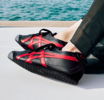 Schwarze und rote Sportschuhe mit einer glatten Lederoberfläche, runder Zehenpartie, strukturierten Sohlen und überkreuzten roten Akzenten.
