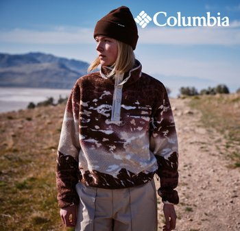Pull en polaire brun et blanc à motifs avec un col haut et une patte de boutonnage. Porté avec un bonnet brun, assorti à un pantalon beige clair.
