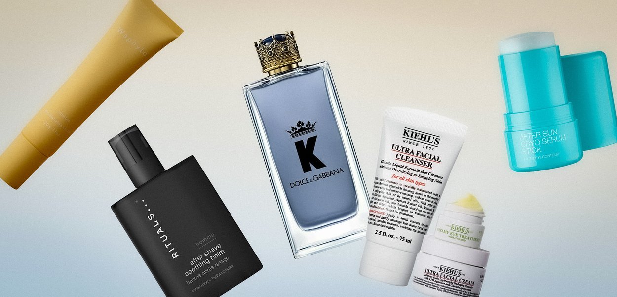 Diversos productos de cuidado de la piel y fragancias que incluyen bálsamo después del afeitado, limpiador facial, crema facial, tratamiento para ojos, perfume y un stick de suero sobre un fondo claro.