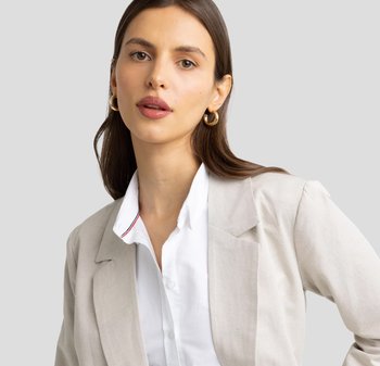Lichtbeige blazer met gestructureerde schouders, gecombineerd met een witte overhemden met een rood en marineblauwe afwerking op de kraag. Gladde textuur.