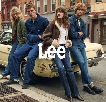 Vier individuen in denim en buitenkleding leunen tegen een vintage gele auto. Verschillende stijlen: groene bomberjack, donkerdenimjacket en een gestructureerde bruine jas.