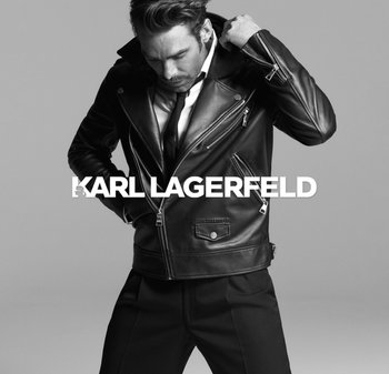 Black leather biker jacket with silver zippers, designed with an asymmetrical front, large lapels, and structured shoulders, worn over a white shirt.