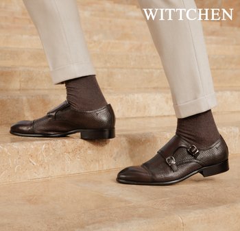 Braune doppelte Monk-Strap-Lederschuhe mit strukturiertem Muster, getragen mit dunklen Socken und beigen Hosen auf Steinstufen.