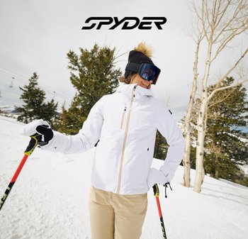 Veste de ski blanche avec un col montant et une fermeture éclair, rehaussée d'un pompon en fourrure sur un bonnet noir. La personne porte des bâtons de ski rouges sur la neige.