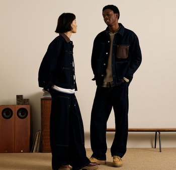 Deux individus portent des vestes en denim bleu marine avec des patchs marron contrastants et des pantalons amples. Les vestes disposent de poches et de boutons en métal.