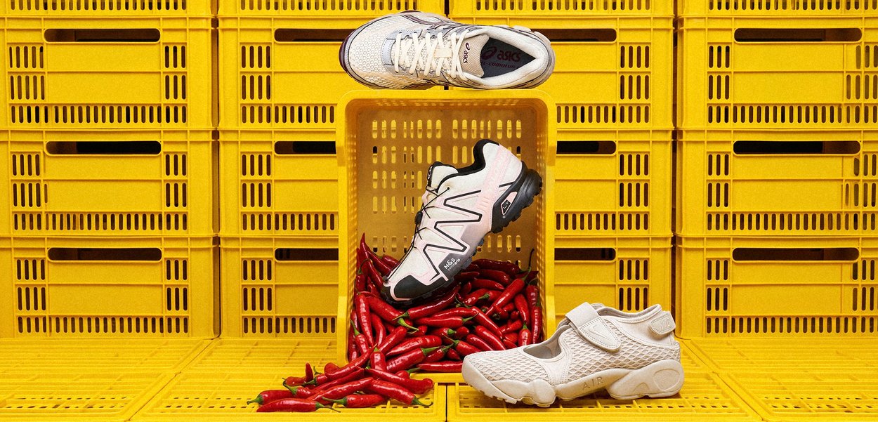 Three white athletic shoes displayed with red chili peppers spilling from a yellow plastic crate background.