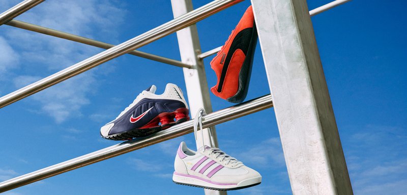 Trois paires de chaussures de sport : des Nike bleu marine et blanches avec des accents rouges, des Puma entièrement rouges et des Adidas gris clair avec des rayures violettes.