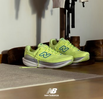 New Balance sneakers in bright yellow with blue accents, mesh upper, cushioned sole, placed on a textured mat near wooden shoes.