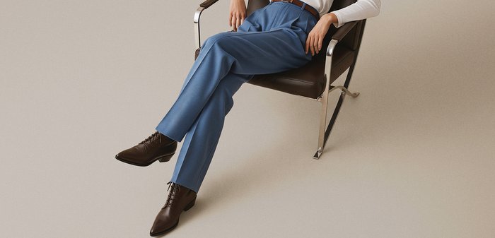 Blue trousers crafted from a smooth fabric, designed with a tailored fit and pleats, complemented by brown leather ankle boots with a pointed toe.