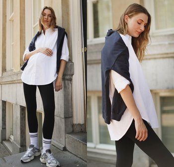 Weißes oversized Hemd, navy Sweatshirt locker drapiert, schwarze Leggings, weiße Socken mit blauen Streifen und graue Sneakers. Urbaner Hintergrund.