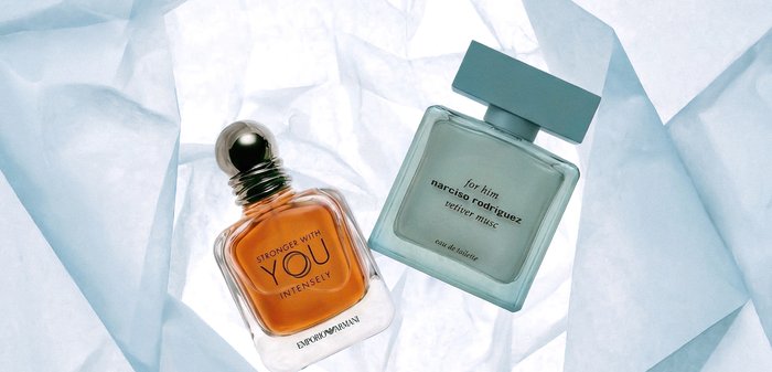 Deux flacons de parfum pour hommes, Emporio Armani Stronger With You Intensely avec un liquide ambré, et Narciso Rodriguez For Him vetiver musk, posés sur un tissu translucide.
