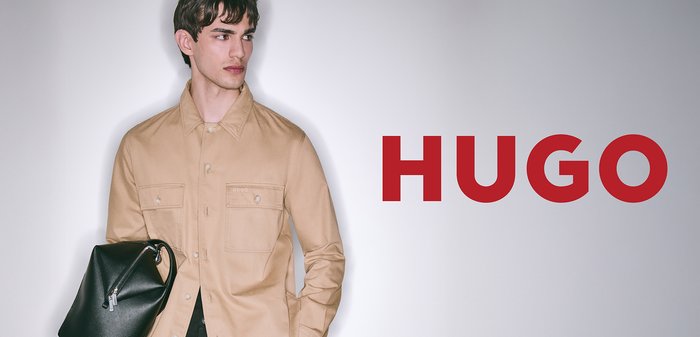 Beige Hemd mit Knöpfen, zwei Brusttaschen und Logoplakette, kombiniert mit einer schwarzen strukturierten Tasche mit Reißverschluss.