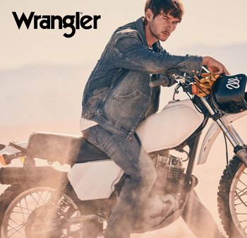 Ung mann iført denimjakke og jeans sitter på en støvete hvit terrengsykkel, og holder en svart hjelm med gule hansker.