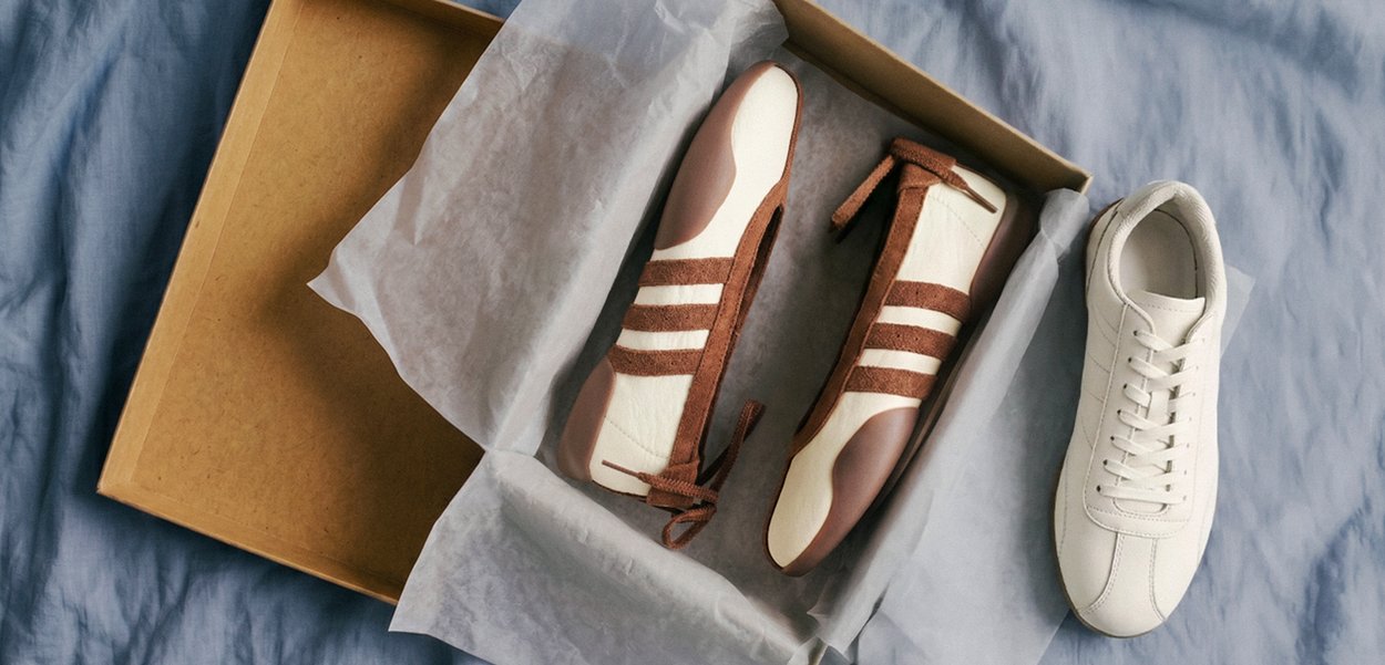 Par de zapatillas retro blancas y marrones en una caja de zapatos abierta con una zapatilla blanca a juego colocada afuera sobre una superficie de tela azul.