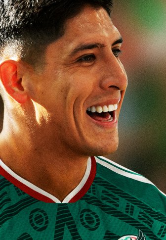 Jeune homme souriant, portant un maillot de sport vert avec des bordures rouges et blanches, probablement lors d'un événement ou d'une célébration de football.