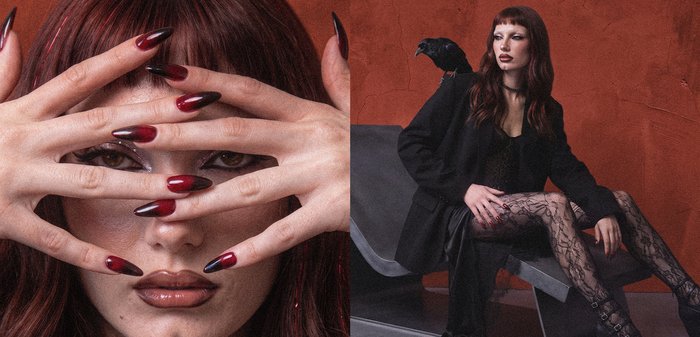Femme aux longs cheveux roux et maquillage sombre montre de longs ongles dégradés rouges et noirs, puis s'assoit sur un banc moderne vêtue de noir avec un oiseau noir sur l'épaule.