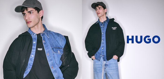 Schwarze Jacke mit auffälligem Logo, über ein blaues Denim-Hemd und ein schwarzes T-Shirt geschichtet, kombiniert mit hellblauen Jeans, vor einem neutralen Hintergrund präsentiert.
