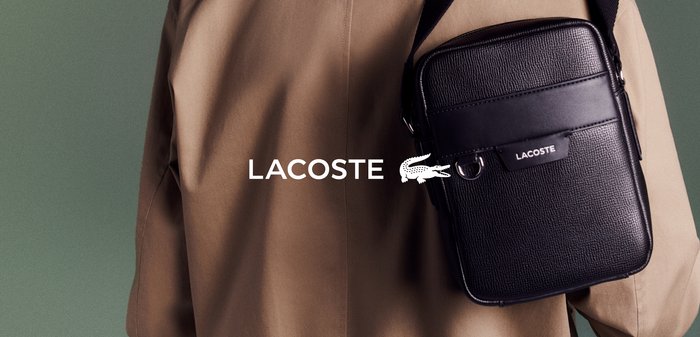 Sac bandoulière en cuir noir avec une finition texturée, doté d'une poche avant, de ferrures argentées et d'un logo Lacoste blanc bien visible.
