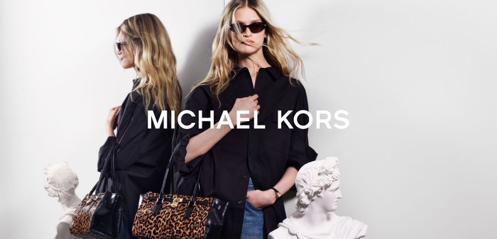 Svart blus, blå jeans och leopardmönstrad handväska. Solglasögon på. Vit byststaty i bakgrunden. Text: "MICHAEL KORS."