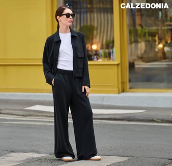 Black relaxed-fit jacket and matching pants, paired with a white t-shirt. Model wears black sunglasses and light-colored shoes.